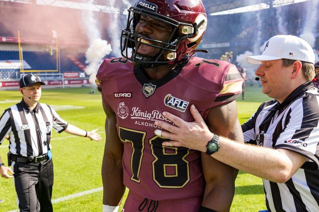 American-Football-Spieler #78 im weinroten Trikot nach dem Spielzug, umgeben von Schiedsrichtern