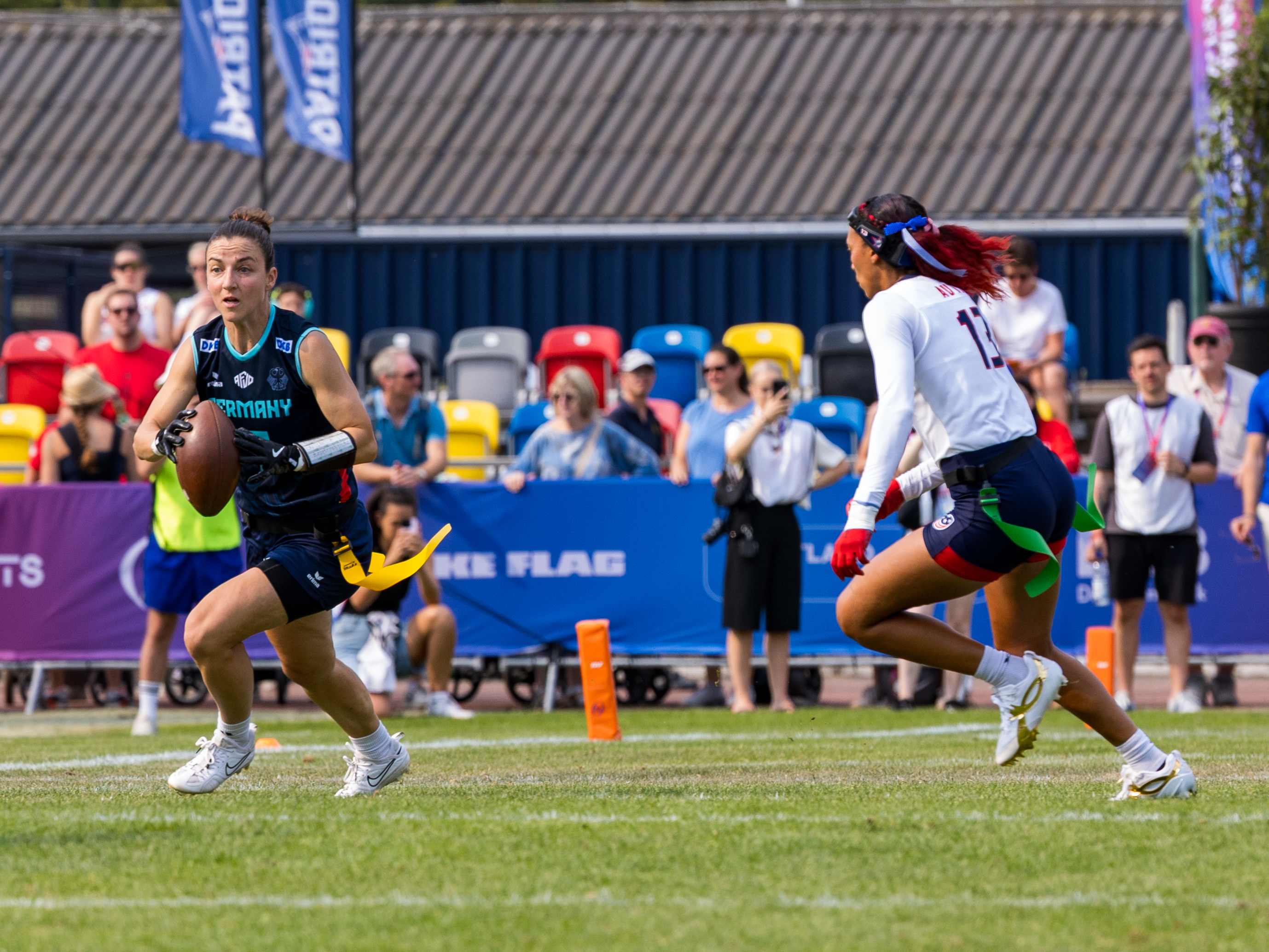 #7 Kyra Fischer (WR/DB) Team Germany Women run with the ball. #13 Deliah Autry (LB/DB) Team USA Women on the way to tackle.