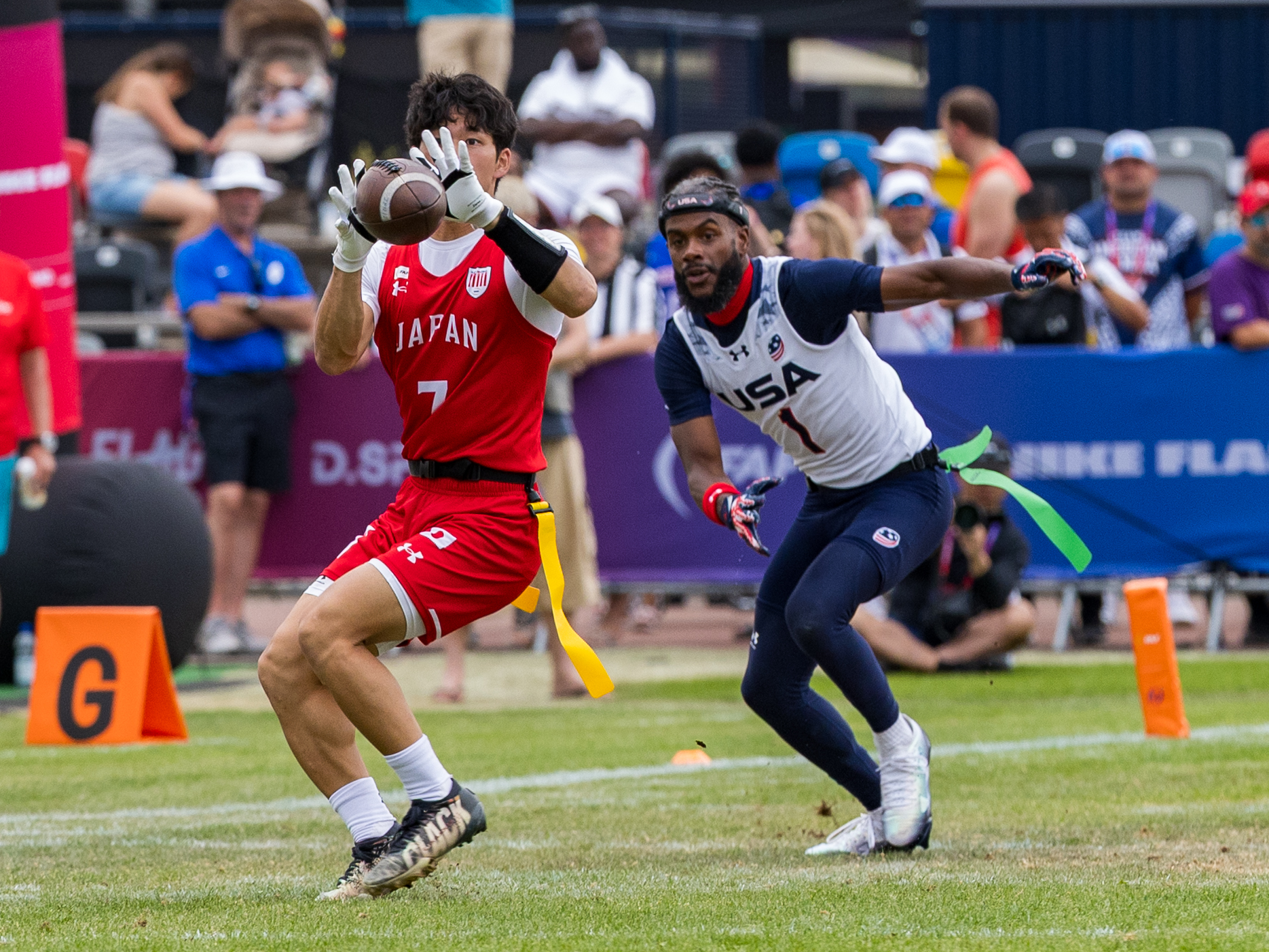 #7 HIROKI UCHIDA ( WR/DB ) Team Japan Men catch the ball in the air. #1 Antonio Coleman (QB/ATH) Team USA Men run to the player.